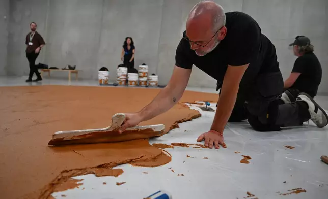 Workers spread peanut butter on a floor to recreate the "Peanut Butter Floor" artwork in tribute to Dutch artist Wim T. Schippers at the Museum Boijmans Van Beuningen in Rotterdam, Netherlands, Friday, July 3, 2026. (AP Photo/Mouneb Taim)