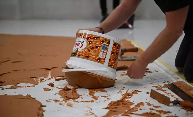 Workers spread peanut butter on a floor to recreate the "Peanut Butter Floor" artwork in tribute to Dutch artist Wim T. Schippers at the Museum Boijmans Van Beuningen in Rotterdam, Netherlands, Friday, July 3, 2026. (AP Photo/Mouneb Taim)