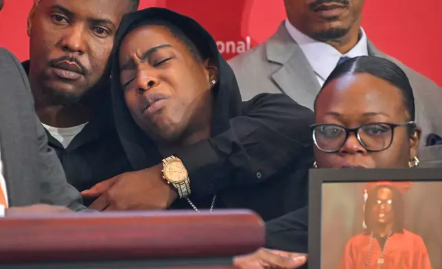 Azariah Mayhorn is comforted by uncle Trevon Petty, left, as her mother, Lynsey Smith, right, holds a photo of her deceased son and Mayhorn's sister, Tyler Smith, as they appear at the National Urban League's annual conference, Thursday, July 30, 2026, in Nashville, Tenn. (AP Photo/John Amis)