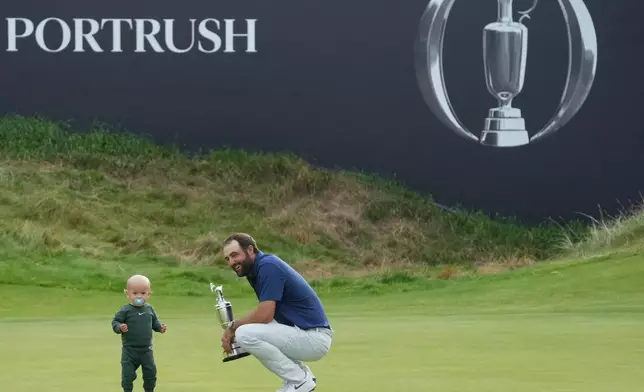 FILE - Scottie Scheffler of the United States holds the Claret Jug trophy as his son, Bennett, stands on the 18th green after winning the British Open golf championship at the Royal Portrush Golf Club, Northern Ireland, July 20, 2025. (AP Photo/Jon Super, File)