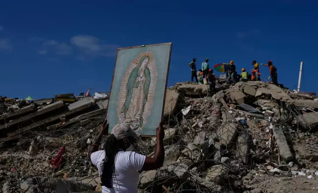 A woman holds a painting of the Virgin Mary as she accompanies a Catholic priest supporting people searching for the remains of relatives in the rubble of residential buildings that collapsed during the earthquakes that struck La Guaira, Venezuela, Friday, July 17, 2026. (AP Photo/Ariana Cubillos)