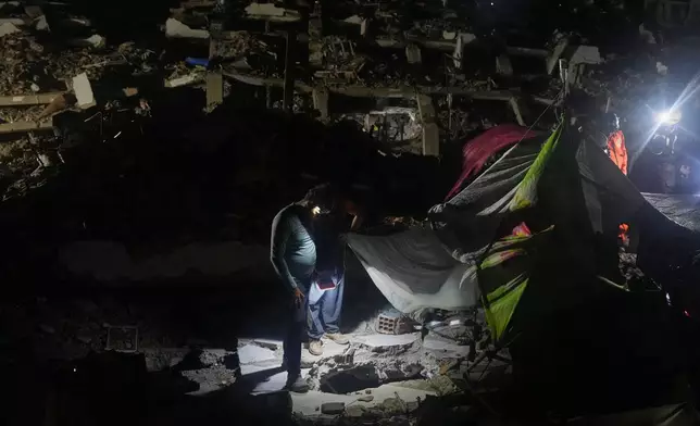 Jerfferson Cova, wearing a headlamp, looks at the deep hole he dug with other relatives in search of his mother-in-law, days after rescuing the bodies of his two children from a building collapsed by an earthquake in La Guaira, Venezuela, Tuesday, July 21, 2026. (AP Photo/Ariana Cubillos)