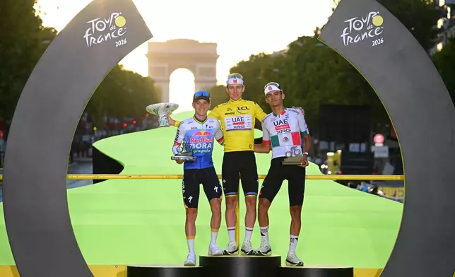 Slovenia's Tadej Pogacar, wearing the overall leader's yellow jersey, celebrates on the podium after winning the Tour de France cycling race alongside Belgium's Remco Evenepoel, second, and Mexico's Isaac Del Toro, third, in Paris, Sunday, July 26, 2026. (AP Photo/Bernard Papon/Pool Photo via AP)