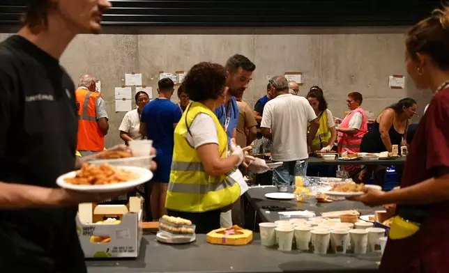 People collect food at a temporary shelter for those displaced by wildfires in Bordeaux, France, Tuesday, July 28, 2026. (AP Photo/Eva van Dam)