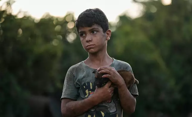 Bashar Hilal, 10, carries a puppy at an animal shelter in the village of Kfaroue, near Nabatiyeh, southern Lebanon, Thursday, July 2, 2026. (AP Photo/Bilal Hussein)