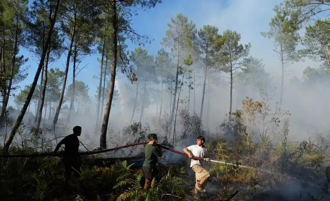 A group hold a firehose and try to suppress a fire near Lacanau, as wildfires rage outside Bordeaux, France, Monday, July 27, 2026. (AP Photo/Baz Ratner)