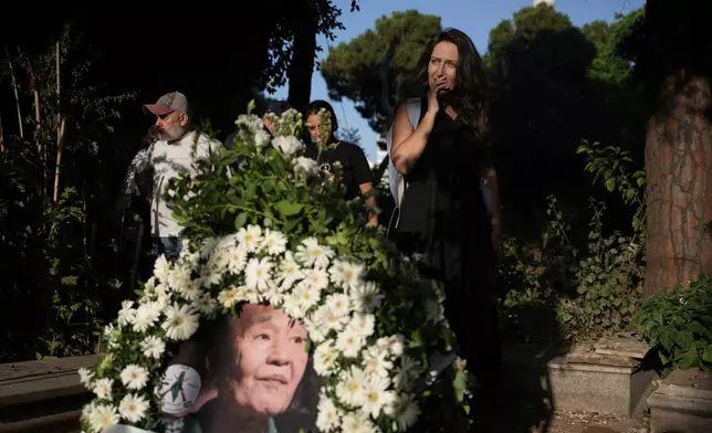 A mourner pays her respects beside a floral wreath bearing a portrait of Kozo Okamoto, a former member of the Japanese Red Army militant group who died Thursday at age 78, at his grave during his burial at Martyrs' Cemetery in Beirut, Lebanon, Friday, July 24, 2026. (AP Photo/Hassan Ammar)