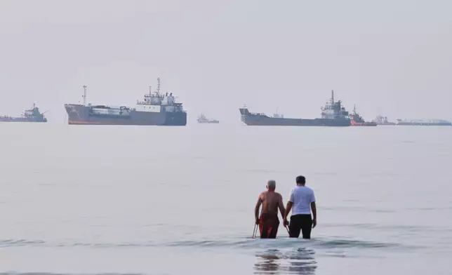 Two men wade in the waters of the Strait of Hormuz with vessels anchored in the background, off Bandar Abbas, Iran, Sunday, July 12, 2026. (Razieh Poudat/ISNA via AP)