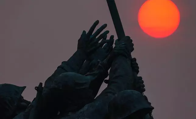 The sun is obscured by wildfire smoke as it rises behind the Marine Corps War Memorial, Friday, July 17, 2026, in Arlington, Va. (AP Photo/Julia Demaree Nikhinson)