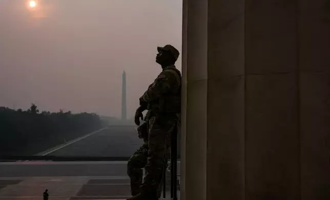 National Guardsmen patrol the Lincoln Memorial as the sun, obscured by wildfire smoke, rises above the Washington Monument and the Reflecting Pool, Friday, July 17, 2026, on the National Mall in Washington. (AP Photo/Julia Demaree Nikhinson)