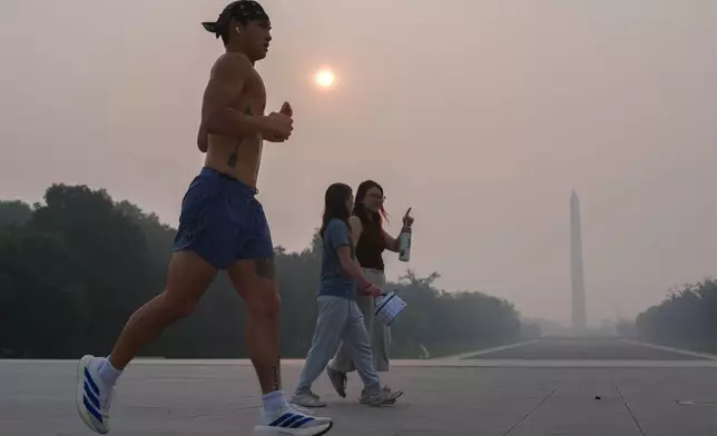 The sun is obscured by wildfire smoke as people run in front of the Washington Monument and Lincoln Memorial Reflecting Pool, Friday, July 17, 2026, on the National Mall in Washington. (AP Photo/Julia Demaree Nikhinson)