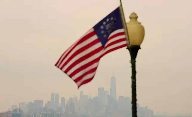 The New York City skyline is shrouded in smoke as a flag flies in a park in Weehawken, N.J., Thursday, July 16, 2026. (AP Photo/Seth Wenig)