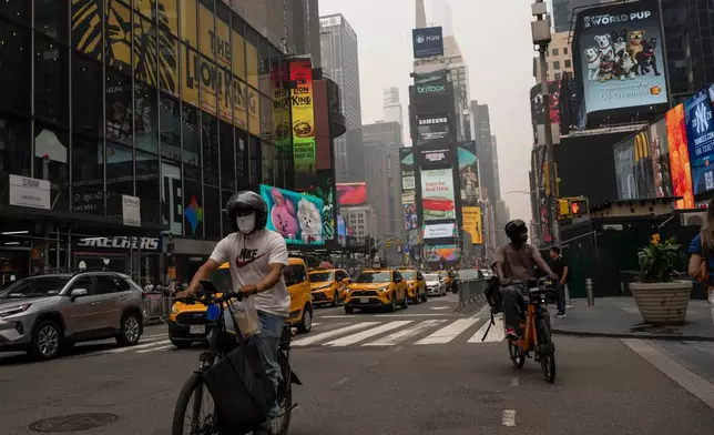 A person wearing a mask cycles in Times Square as smoke from wildfires blankets the sky, Thursday, July 16, 2026, in New York. (AP Photo/Yuki Iwamura)