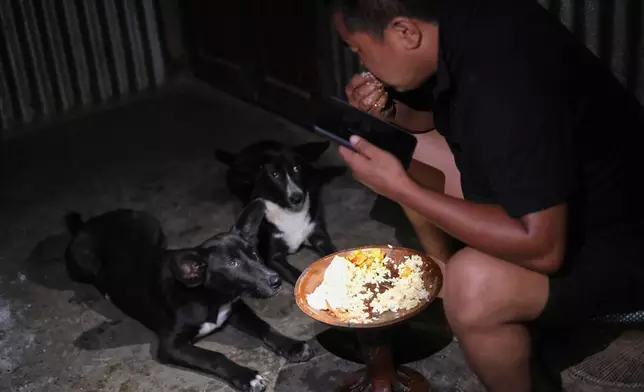 Tovi Murru, 32, eats dinner watched by his dogs inside their kitchen in Kohima, capital of the northeastern Indian state of Nagaland, Monday, July 6, 2026. (AP Photo/Yirmiyan Arthur)