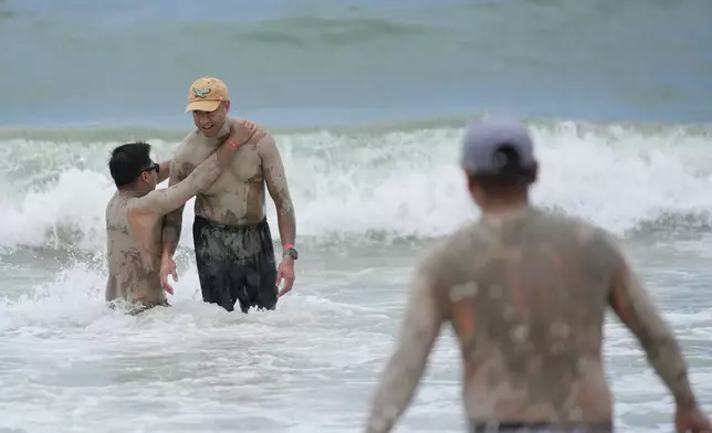 Visitors who are covered in mud during the Boryeong Mud Festival play at a beach in Boryeong, South Korea, Saturday, July 25, 2026. (AP Photo/Lee Jin-man)