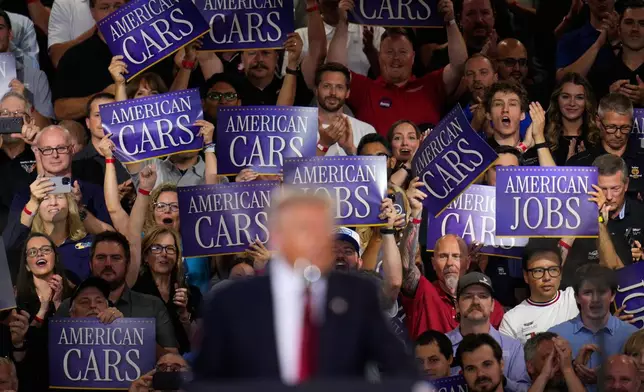 Attendees hold signs as President Donald Trump speaks at the General Motors Proving Ground, Monday, July 27, 2026, in Milford, Mich. (AP Photo/Paul Sancya)