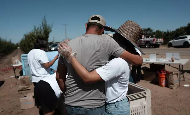 Cesar Mora, left, and his wife, Juliana, hug after a free nectarine giveaway at Mora's orchard in Reedley, Calif., Wednesday, July 1, 2026. (AP Photo/Jae C. Hong)