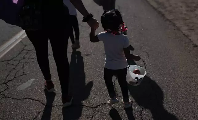 Elianna Ealey holds her mother's hand while carrying a small bucket with nectarines during a free giveaway at Cesar Mora's orchard in Reedley, Calif., Wednesday, July 1, 2026. (AP Photo/Jae C. Hong)
