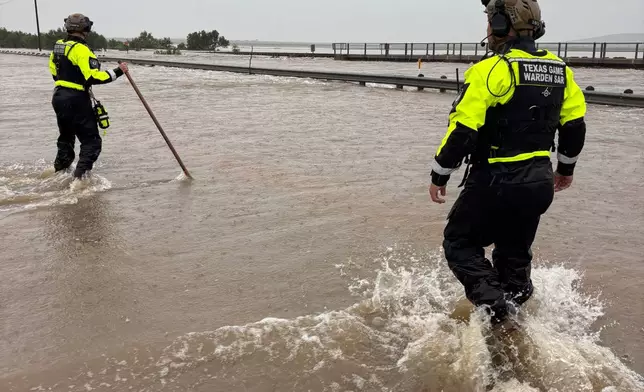 In this handout photo provided by the Texas Parks and Wildlife Department, game wardens walk through high waters from heavy rains in Uvalde County, Texas, on Tuesday, July 14, 2026. (Texas Parks and Wildlife Department via AP)
