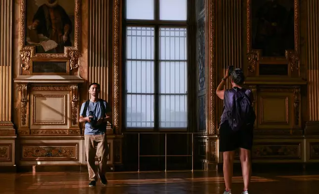 Visitors take a picture of the window which was broken during the reopening to the public of the Apollo Gallery, at the Louvre museum in Paris, Wednesday, July 22, 2026. (Lou Benoist/Pool Photo via AP)