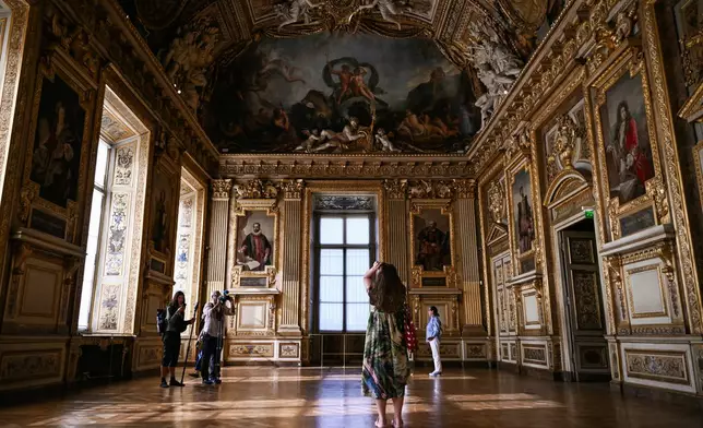 Visitors take a picture of the window which was broken during the reopening to the public of the Apollo Gallery, at the Louvre museum in Paris, Wednesday, July 22, 2026. (Lou Benoist/Pool Photo via AP)