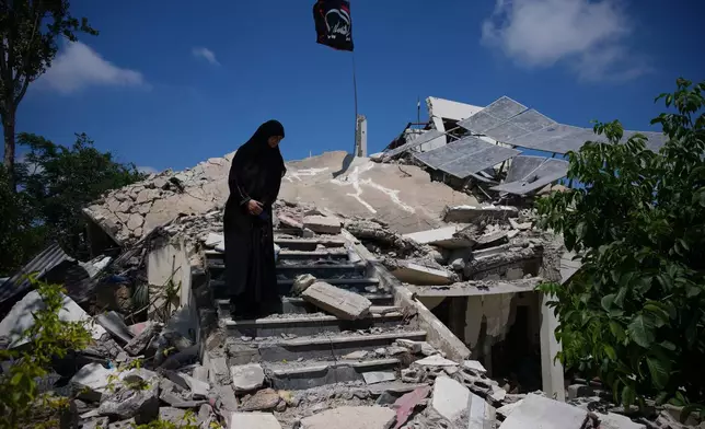 Fatima Mokdad stands amid the rubble of her home, which was destroyed in an Israeli airstrike during the Israel-Hezbollah war, where she and her family continue to live, using the only room that remained intact, in Froun village, southern Lebanon, Tuesday, July 21, 2026. (AP Photo/Hassan Ammar)