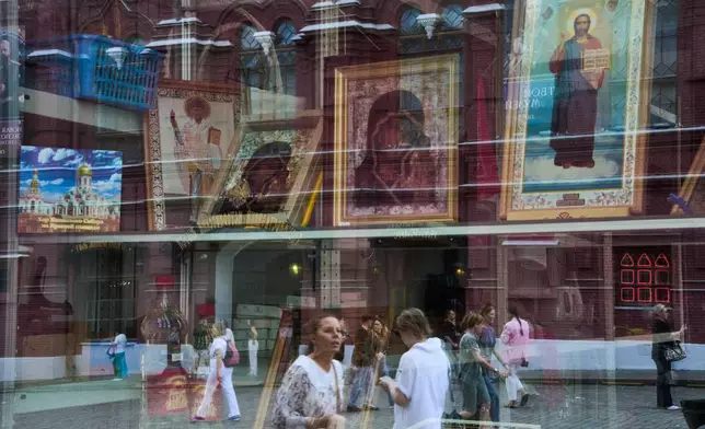 People are reflected in the window of an icon shop on Red Square near the Church of the Kazan Icon of the Mother of God in Moscow on Tuesday, July 21, 2026, the feast day of the Kazan Icon of the Mother of God. The Kremlin Wall and the Spasskaya Tower are in the background at left. (AP Photo/Alexander Zemlianichenko)
