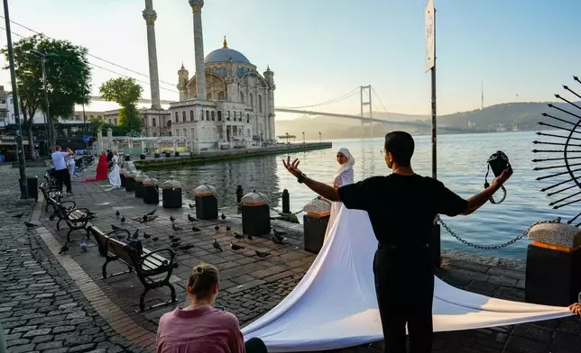 Photographer Enes Khazam works during a photo session on the bank of the Bosphorus Strait, with the Ortakoy mosque and 15th July Martyrs bridge in the background in Istanbul, Turkey, early Friday, June 26, 2026. (AP Photo/Emrah Gurel)