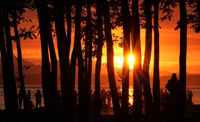 The sun sets over Golden Gardens Park as people gather on the beach Wednesday, July 15, 2026, in Seattle. (AP Photo/Lindsey Wasson)