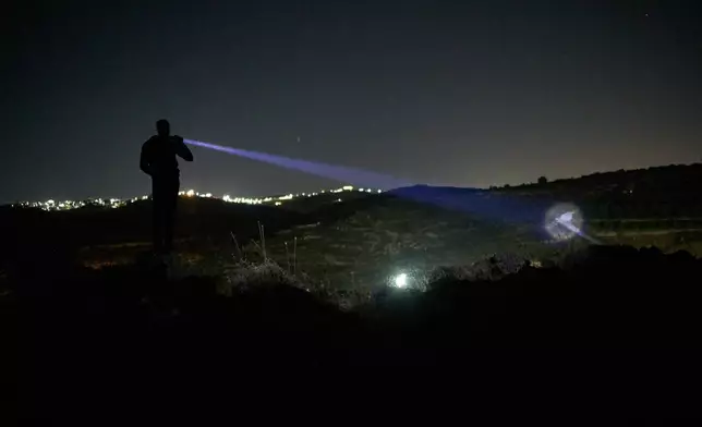 A Palestinian uses a flashlight as he takes part in a night watch to protect their village against Israeli settler attacks in the West Bank village of Sinjil, Thursday, July 16, 2026. (AP Photo/Leo Correa)