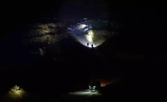 Palestinians use flashlights after spotting the presence of Israeli settlers on a hill as they take part in a night watch to protect their West Bank village of Sinjil, Thursday, July 16, 2026. (AP Photo/Leo Correa)