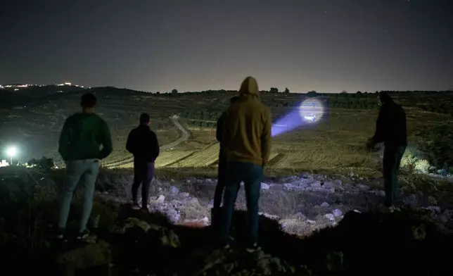 A Palestinian uses a flashlight after spotting Israeli settlers on a nearby hill while taking part in a night watch with other volunteers to guard against settler attacks on the West Bank village of Sinjil, Thursday, July 16, 2026. (AP Photo/Leo Correa)