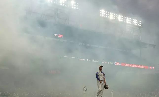Smoke drifts as Chicago Cubs first baseman Michael Busch looks on after fireworks before a baseball game against the St. Louis Cardinals, Saturday, July 4, 2026, in Chicago. (AP Photo/David Banks)