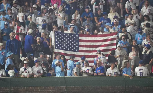 Fans hold a United States flag in the bleachers during the sixth inning of a baseball game between the Chicago Cubs and the St. Louis Cardinals, Saturday, July 4, 2026, in Chicago. (AP Photo/David Banks)