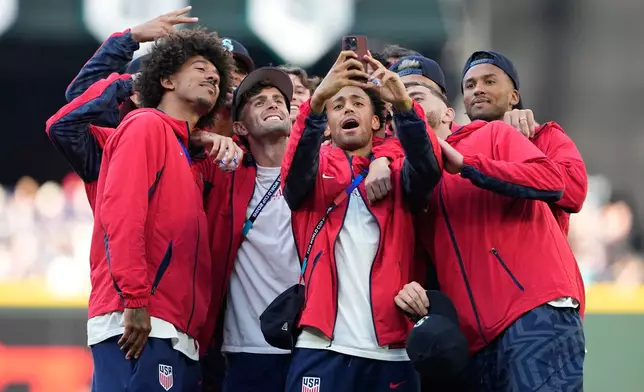 From left, United States men's national soccer team players Chris Richards, Christian Pulisic, Tyler Adams and Matt Turner take a photo with teammates on the field before a baseball game between the Seattle Mariners and the Toronto Blue Jays, Friday, July 3, 2026, in Seattle. (AP Photo/Lindsey Wasson)