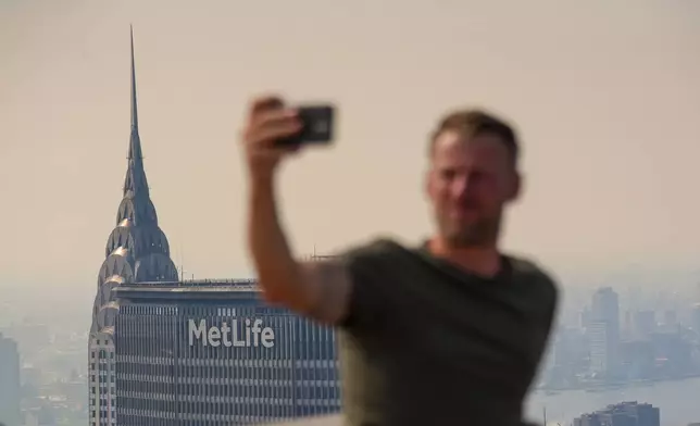 A person takes a selfie from the Top of The Rock observation deck at the Rockefeller Center during an air quality health advisory due to wildfire smoke, in New York, Friday, July 17, 2026. (AP Photo/Ryan Murphy)