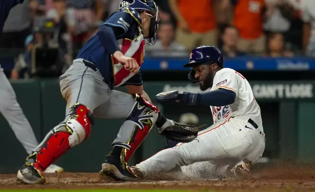 Houston Astros' Taylor Trammell, right, beats a tag by Tampa Bay Rays catcher Hunter Feduccia, left, to score on a sacrifice fly by designated hitter Yordan Alvarez during the seventh inning of a baseball game in Houston, Saturday, July 4, 2026. (AP Photo/Jon Shapley)