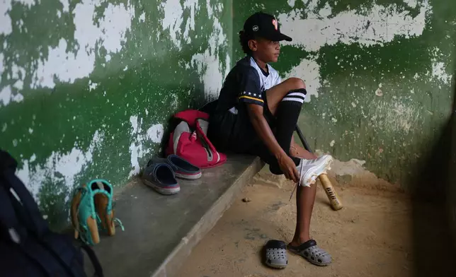 Yeferson Seijas puts his cleats on for baseball practice in La Guaira, Venezuela, Saturday, July 11, 2026, after the earthquakes left his family without a home and some of the boys he grew up playing with injured, orphaned, dead or missing. (AP Photo/Ariana Cubillos)