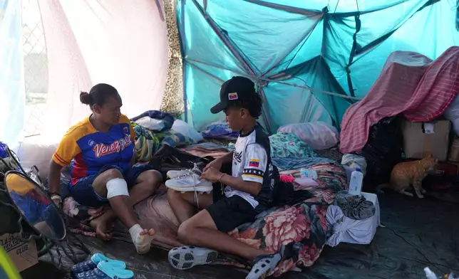 Yeferson Seijas sits with his mother Elizabeth Pacheco inside the tent where they have been staying since the earthquakes displaced their family, before leaving for baseball practice in La Guaira, Venezuela, Saturday, July 11, 2026. (AP Photo/Ariana Cubillos)