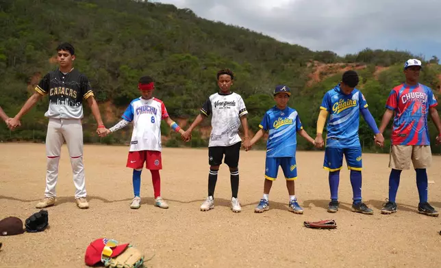 Yeferson Seijas, third from left, joins fellow players in a prayer for those who died in the earthquakes, including some of their baseball mates, before a friendly baseball game on a baseball field in La Guaira, Venezuela, Saturday, July 11, 2026. (AP Photo/Ariana Cubillos)