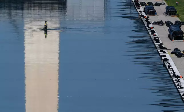 A worker wades through the Lincoln Memorial Reflecting Pool as crews install fireworks ahead of the America 250 July 4th celebration on the National Mall, Thursday, July 2, 2026, in Washington. (AP Photo/Nathan Howard)