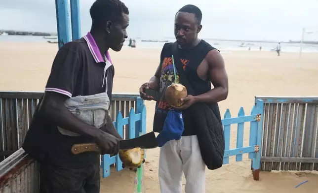 Mukthar Oladunmade, a 27-year-old writer, right, buys a coconut at Takwa Bay beach in Lagos, Nigeria, Sunday, June 28, 2026. (AP Photo/Sunday Alamba)