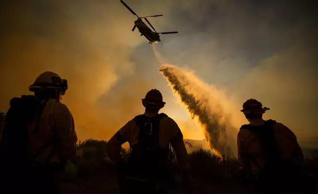 Firefighters watch as a helicopter drops water on the Summit Fire in Llano, CA. Friday, July 10, 2026. (AP Photo/Ethan Swope)