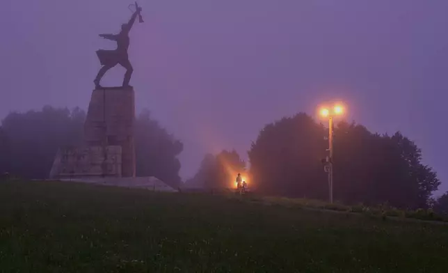 A couple stand near the monument "Peremilovskaya Heights", in Peremilovo village, about 70 kilometers ( 44 miles) north from Moscow, Russia, before sunrise, Sunday, July 12, 2026. (AP Photo/Alexander Zemlianichenko)