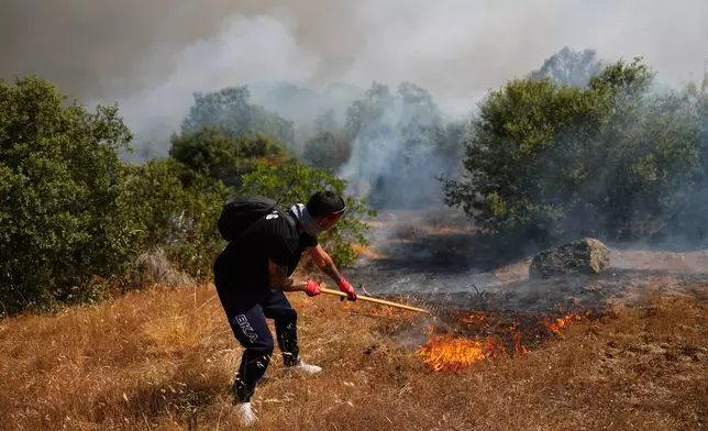 FILE - A volunteer uses a rake trying to help stop a wildfire from advancing in San Martin de Valdeiglesias, west of Madrid, Spain, July 26, 2026. (AP Photo/Manu Fernandez, File)
