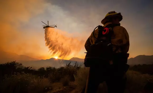 FILE - A firefighter watches as a helicopter drops water on the Summit Fire while battling wildfires in Llano, Calif., July 10, 2026. (AP Photo/Ethan Swope, File)