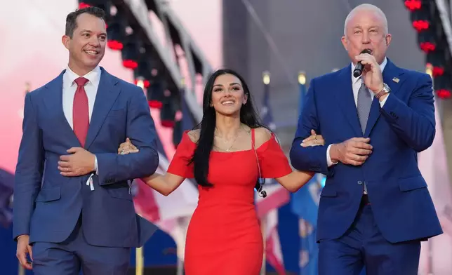 U.S. Ambassador to Belgium Bill White, right, and his husband Bryan Eure, left, walk U.S. country music singer Alexis Wilkins onto the stage during the America 250 event in Brussels, Sunday, June 28, 2026. (AP Photo/Virginia Mayo)