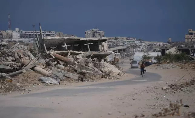 A Palestinian man rides his bicycle by the rubble of buildings that were destroyed during the Israel Hamas war, in Khan Younis, southern Gaza Strip, Friday, July 31, 2026. (AP Photo/Abdel Kareem Hana)