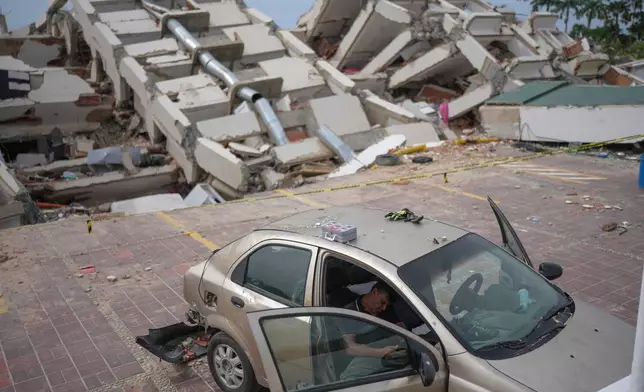 A volunteer helping remove debris from buildings damaged by the earthquakes rests on a damaged car in La Guaira, Venezuela, Friday, July 3, 2026. (AP Photo/Matias Delacroix)