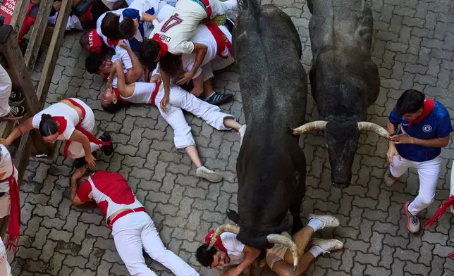 Revelers fall next to Jose Escolar's fighting bulls during the fifth running of the bulls at the San Fermín festival in Pamplona, Spain, Saturday, July 11, 2026. (AP Photo/Miguel Oses)